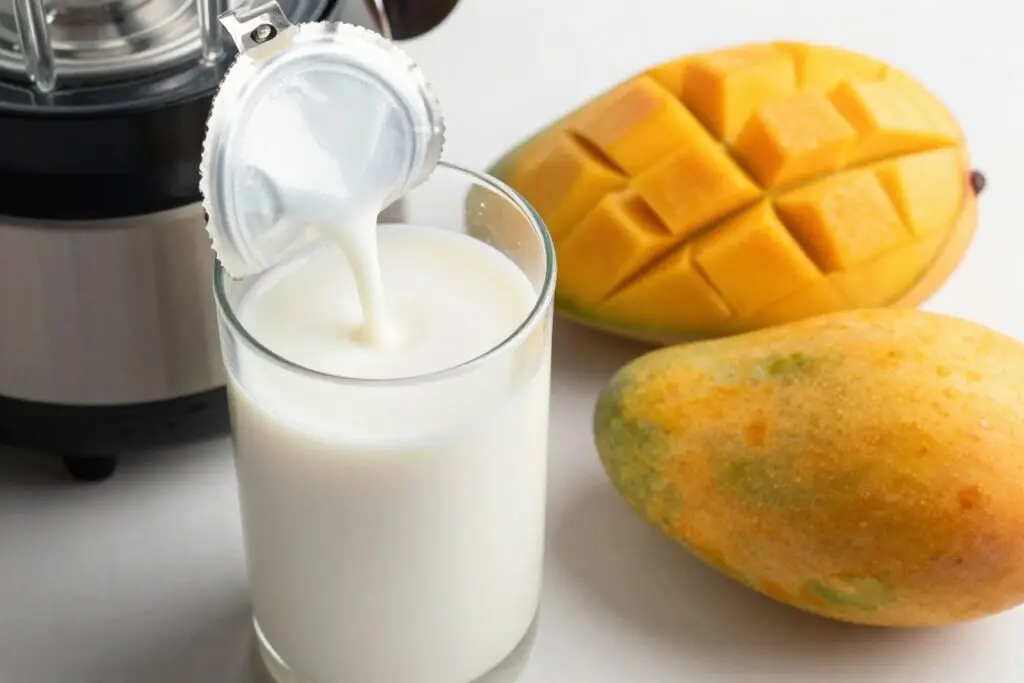 Puszka mleczka kokosowego i świeże mango obok blendera