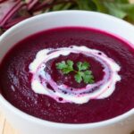 Zupa krem z pieczonego buraka w białej misce z dodatkiem śmietany i świeżych ziół