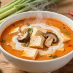 Zupa tajska Tom Yum z tofu w tradycyjnej tajskiej misce z aromatycznymi składnikami dookoła